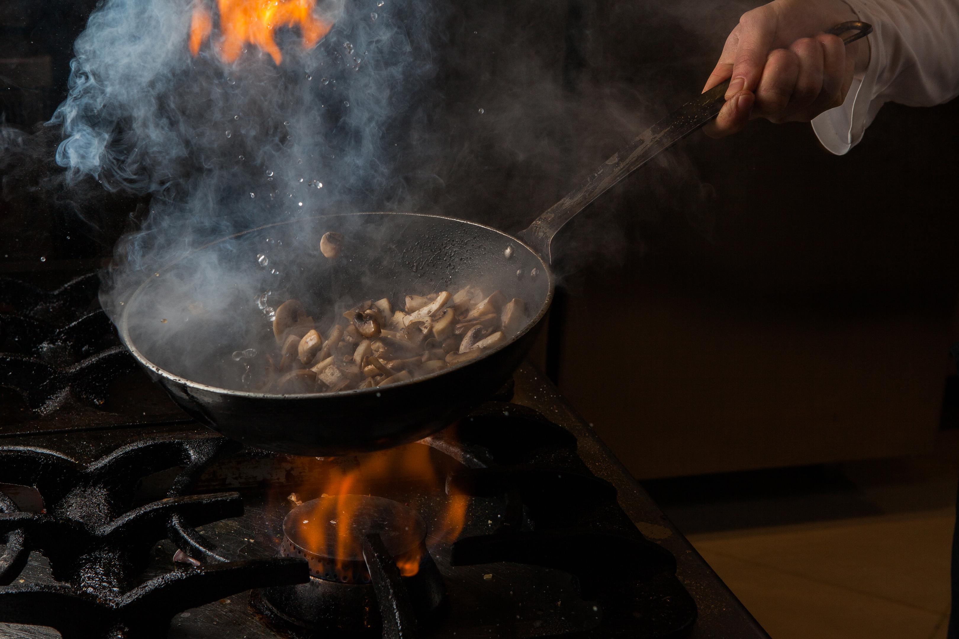 A human hand holding a frypan over a gas stove