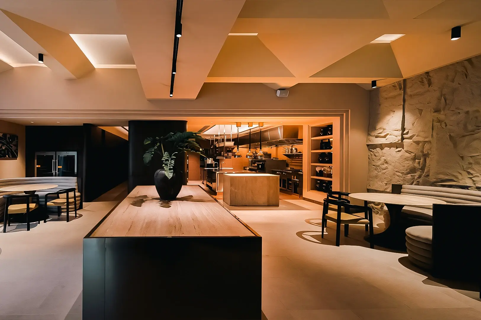 Centered eye‑level wide‑angle shot of a contemporary chef’s table restaurant interior, highlighting warm lighting, open kitchen shelving, textured walls, and refined minimalist décor.