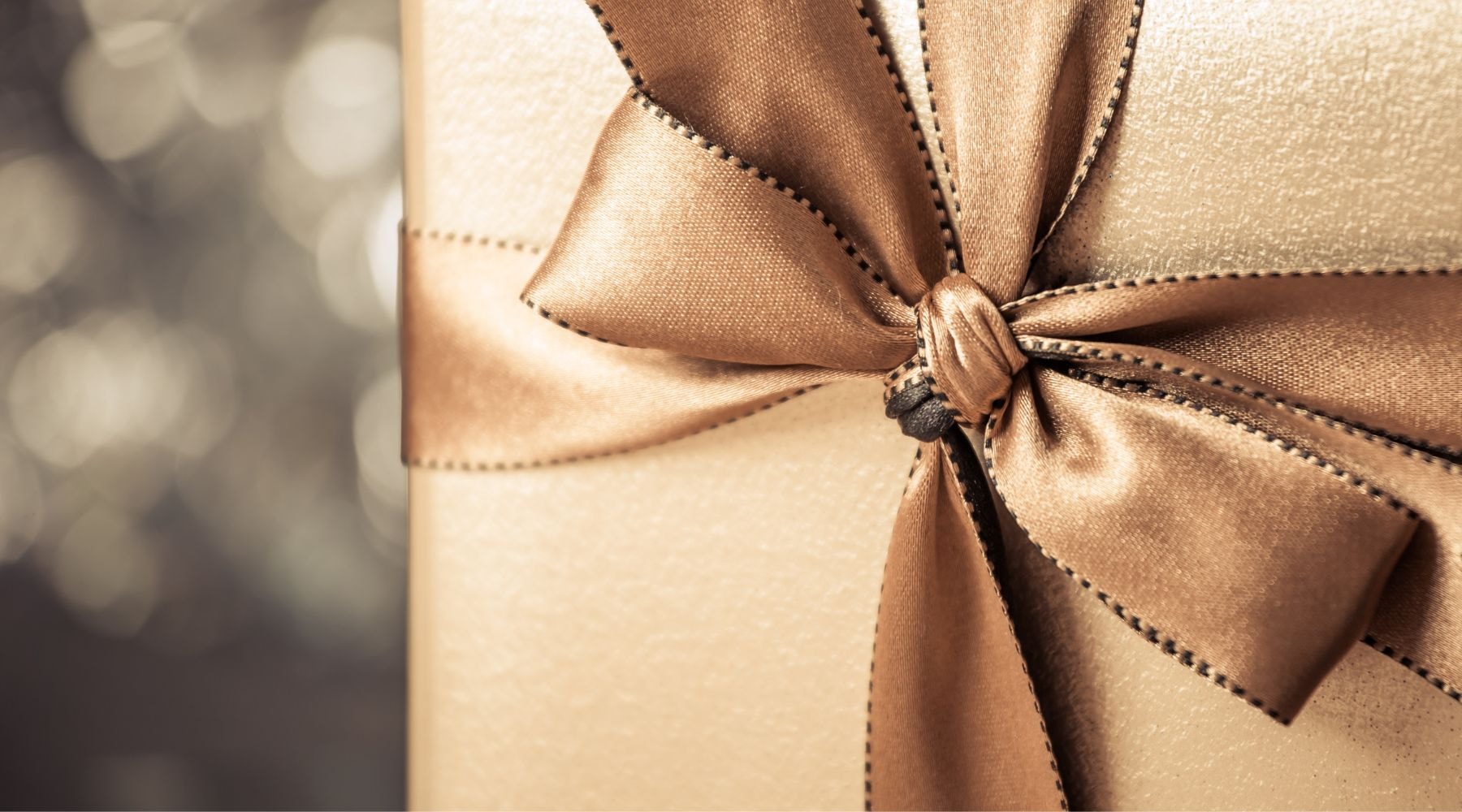 Close-up of a gold gift box featuring a detailed satin bow, set against a softly blurred background.