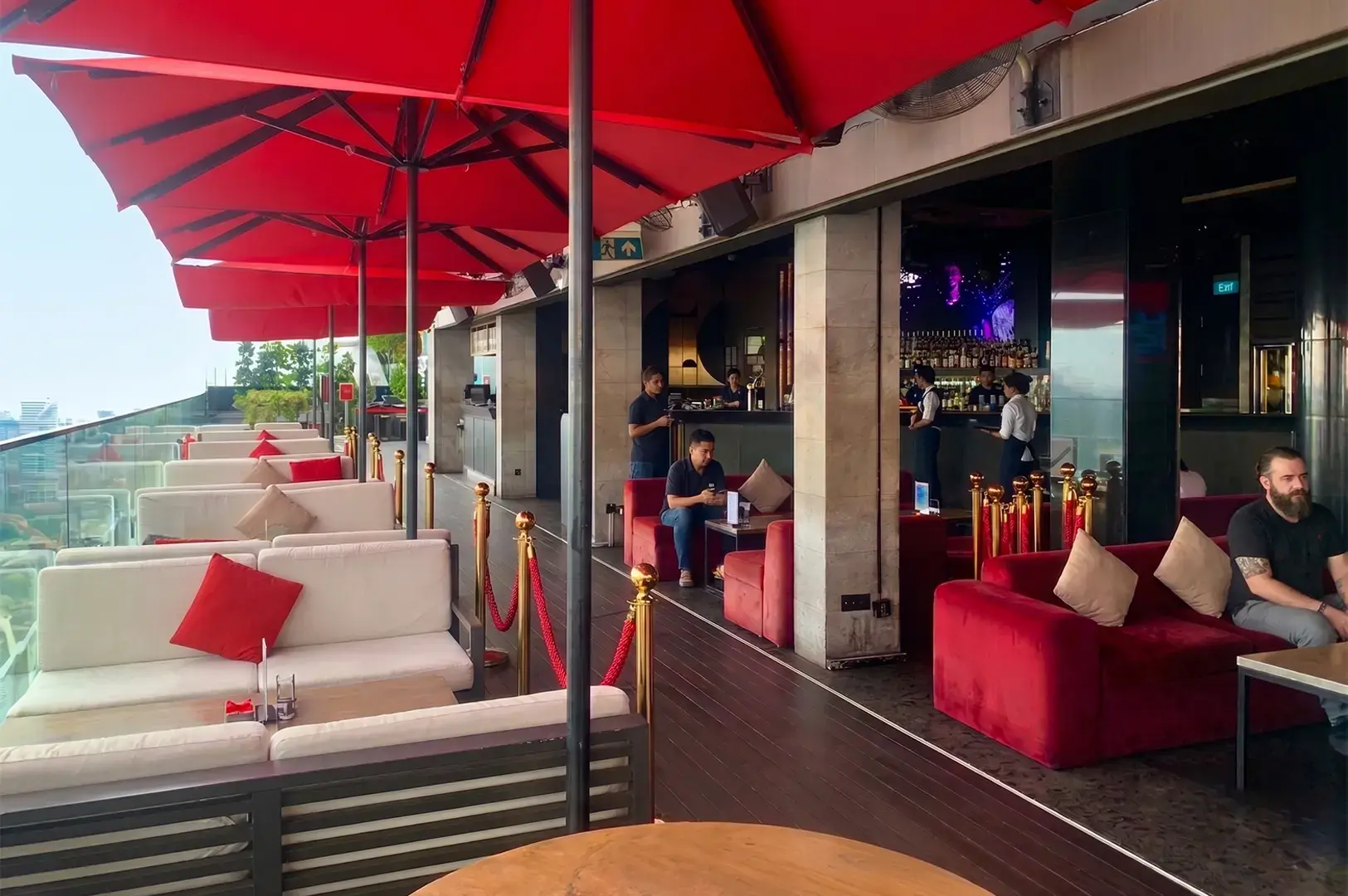 Rooftop bar lounge with red umbrellas, comfortable seating, and city view.