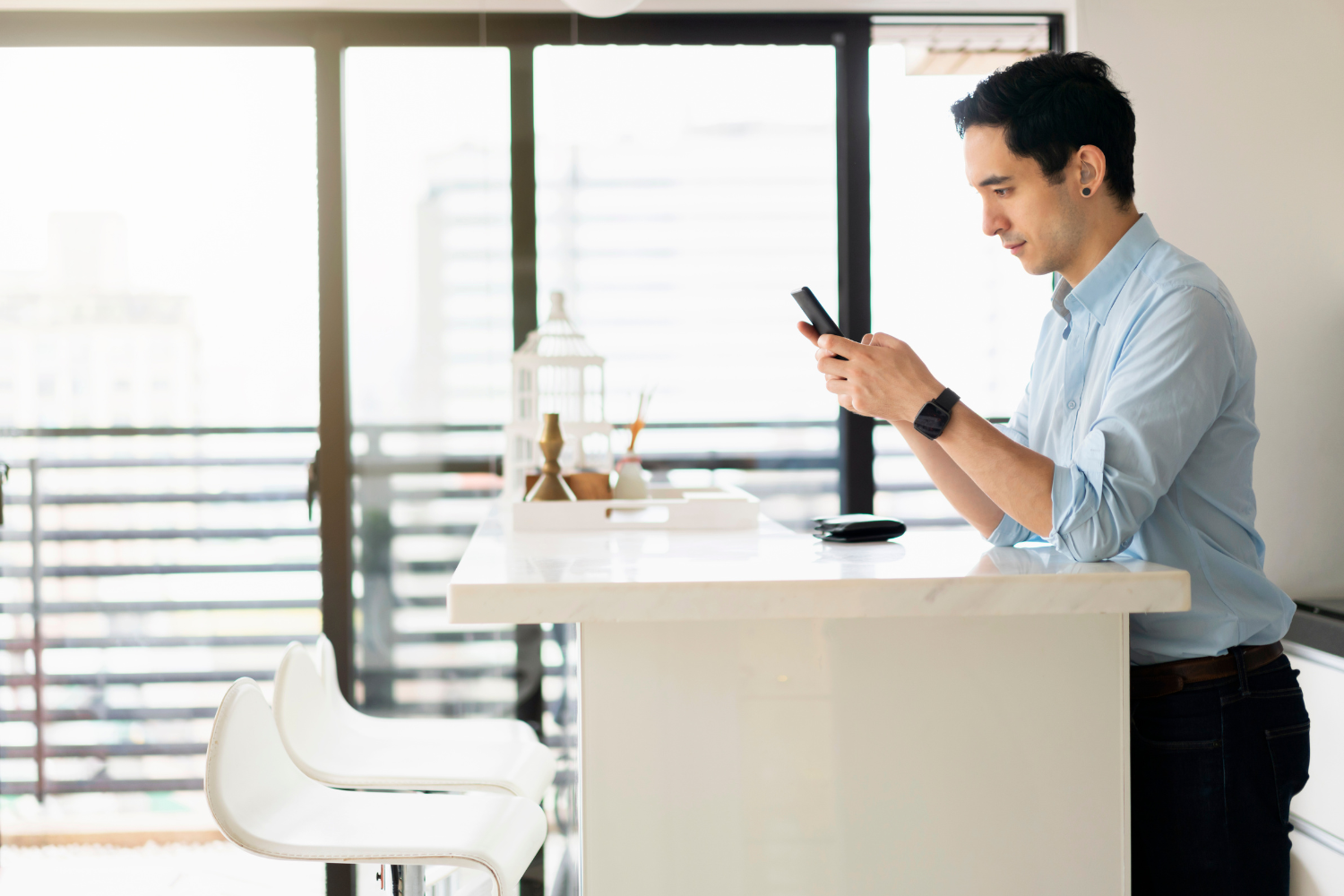 A professional sitting on his dek while typing something on his smartphone.