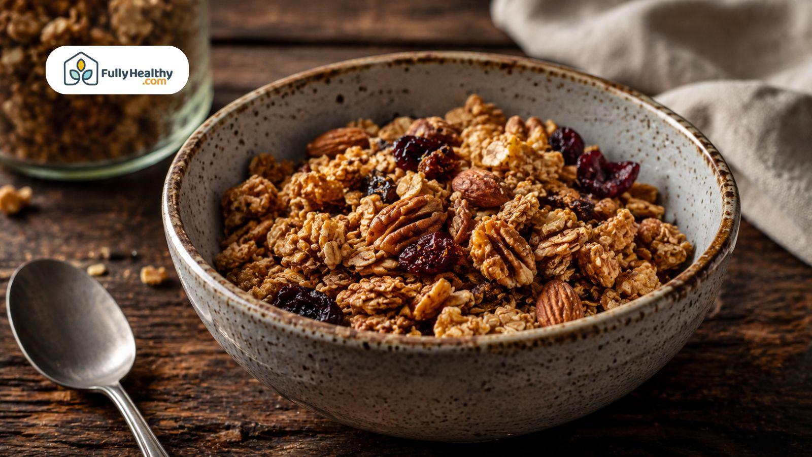 Bowl of granola cereal with oats, pecans, and dried cranberries on a rustic wooden table.