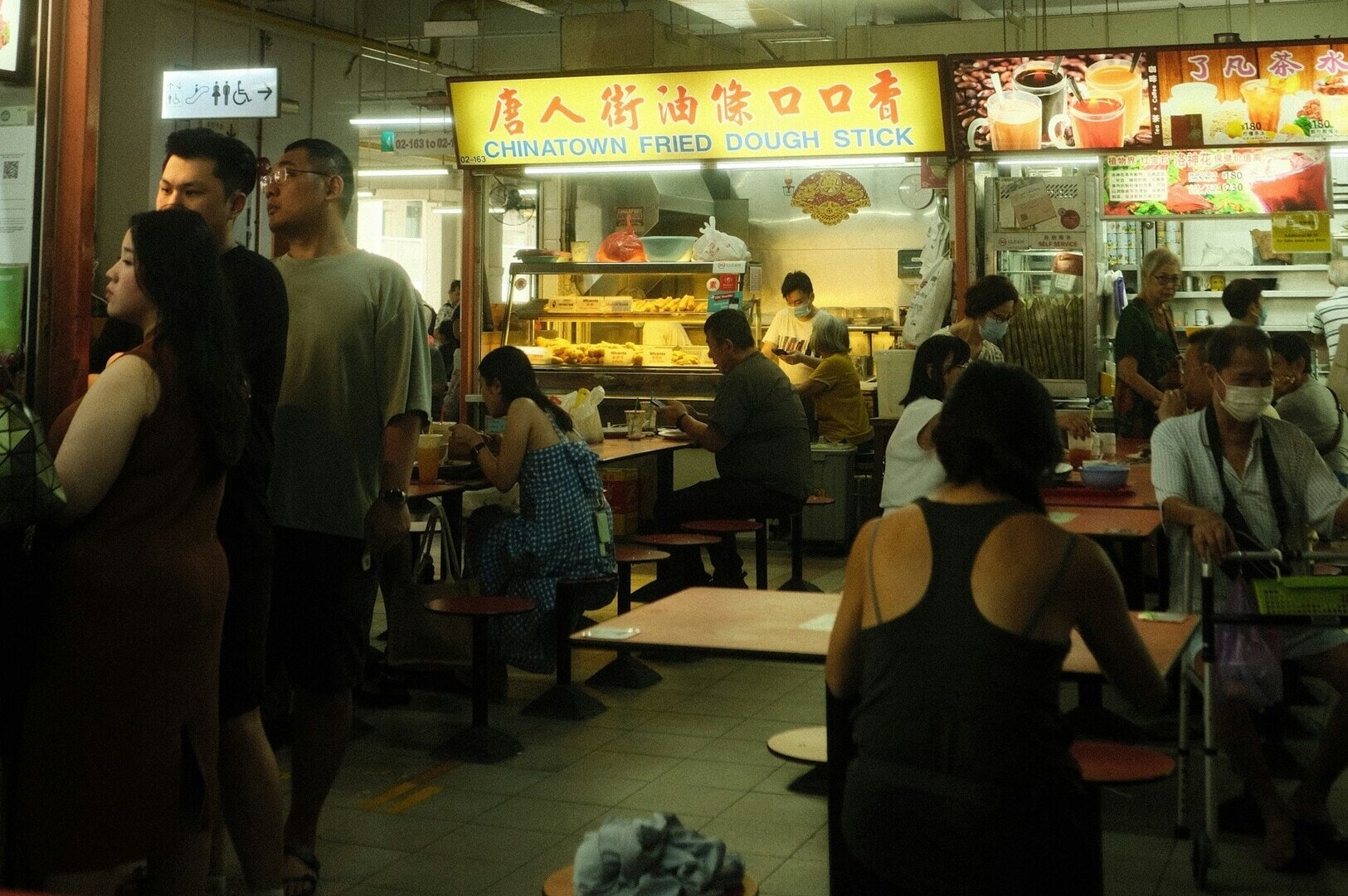 Diners enjoying meals at a bustling Singapore Hawker center, surrounded by various food stalls and vibrant atmosphere.