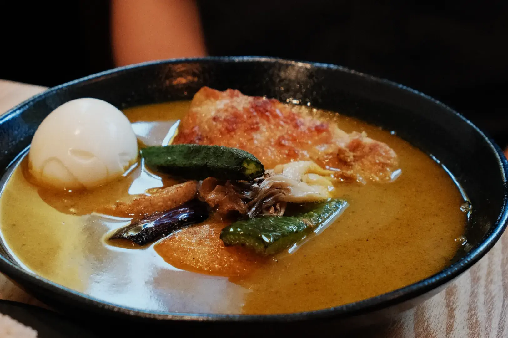 A bowl of curry ramen featuring a soft-boiled egg, various vegetables, and pieces of meat in a rich broth.