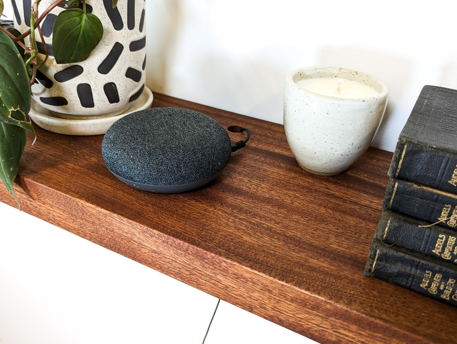 Mahogany floating wall shelves with cord management. Black books rest to the side, a geometric potted vase holds a green plant 