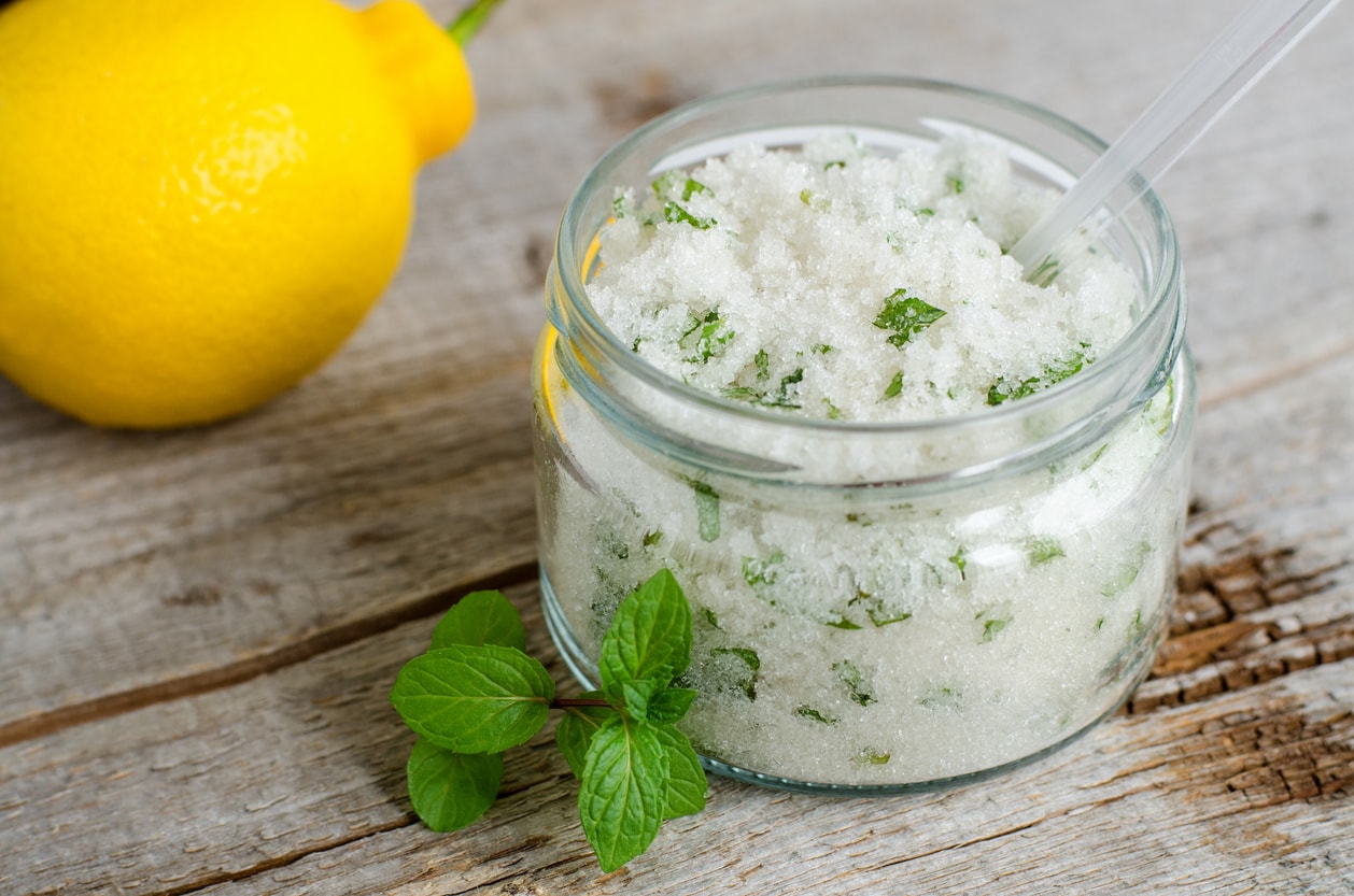 Citrus mint sugar scrub in glass jar with fresh lemon and mint leaves on rustic wooden table, natural homemade body exfoliant