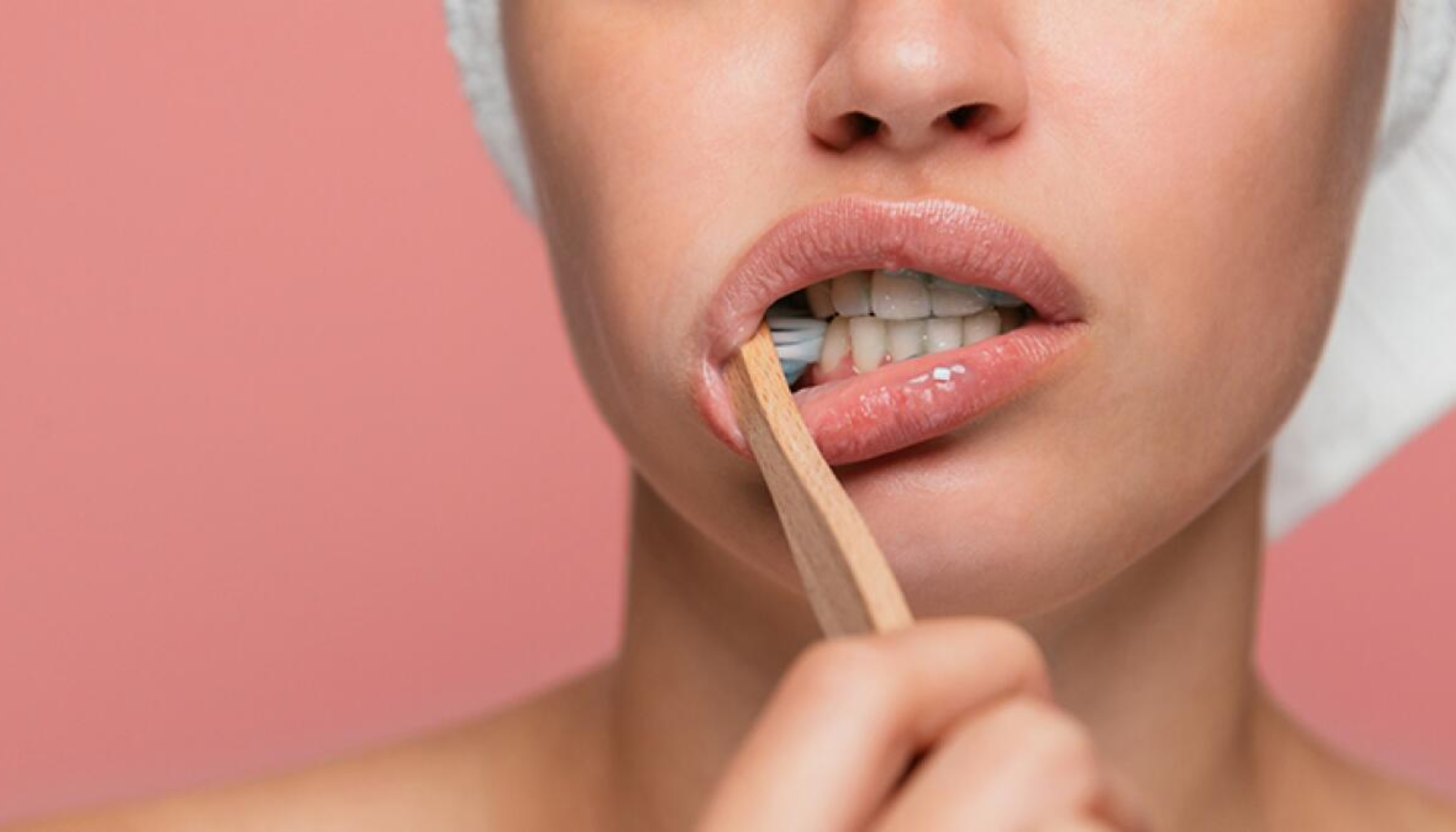 Hvitt Belegg På Tunga? Dette Kan Kroppen Din Prøve Å Fortelle Deg 17 Kvinne pusser tennene med en bambustannbørste foran rosa bakgrunn, fokus på munnhygiene og bærekraftig valg.