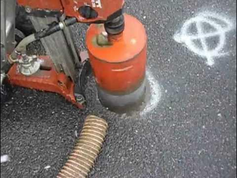 A person setting up a drill to drill a hole in asphalt