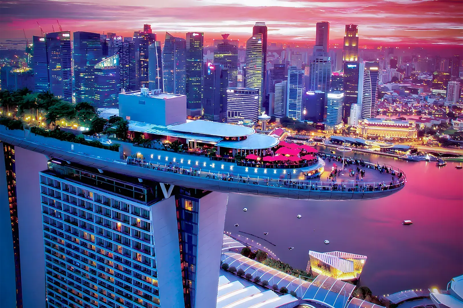 A stunning cityscape at sunset features a towering skyscraper with a rooftop garden and observation deck overlooking a vibrant skyline and waterfront.