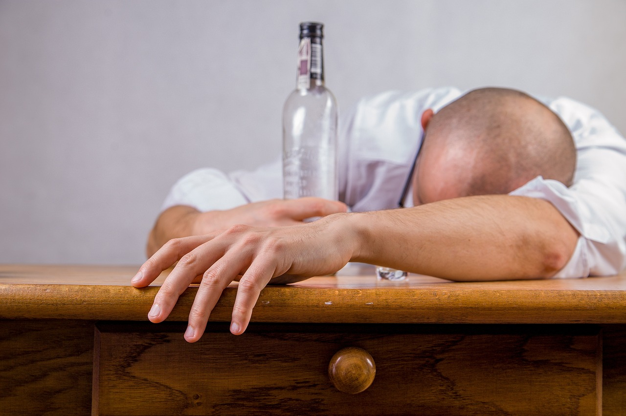An image of a man with an empty wine bottle laying his head on the desk thinking he needs to limit alcohol intake. 