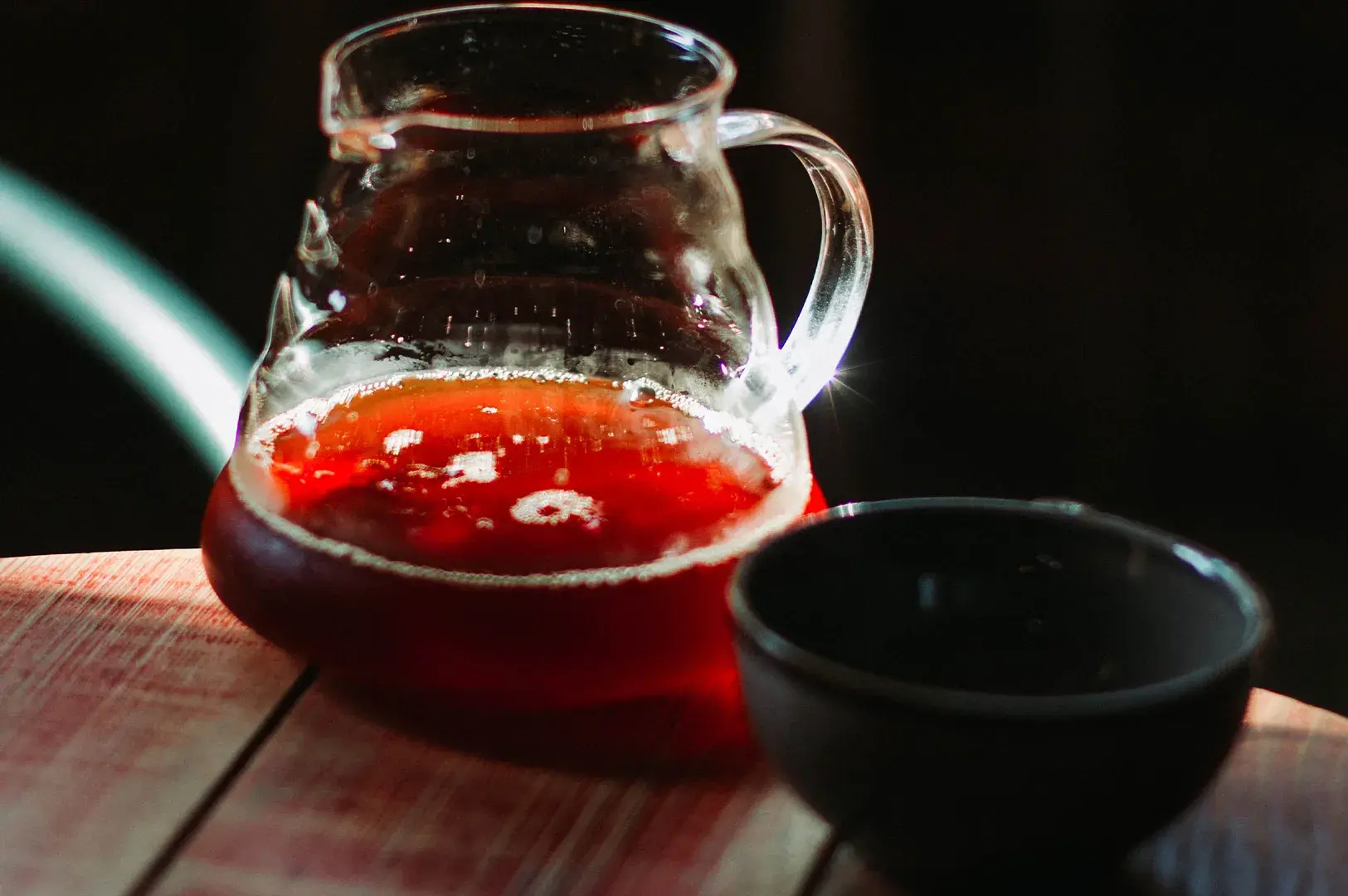Glass decanter with brewed tea beside a black ceramic cup.