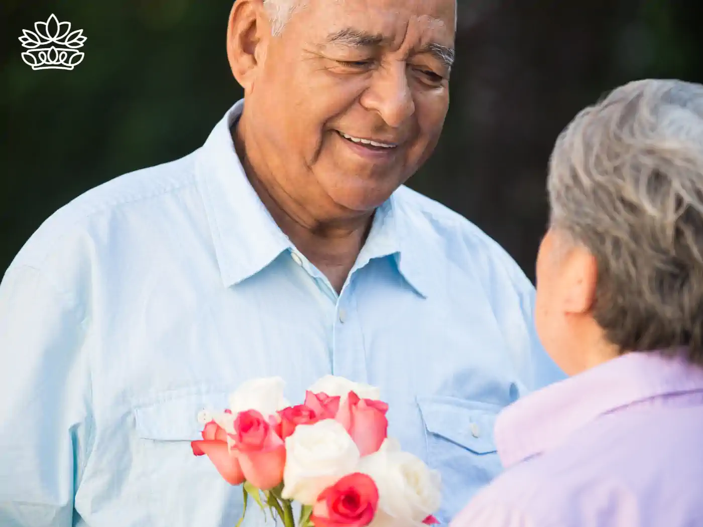 Senior man with a gentle smile presenting a bouquet of red and white roses to his wife, expressing affection in a tranquil outdoor setting. Just Because Flowers. Delivered with Heart. Fabulous Flowers and Gifts