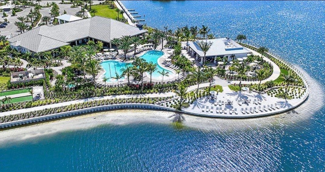 A breathtaking aerial view showcases the Esplanade Lake Club in Fort Myers, Florida, featuring luxury homes with tile roofs and private boat docks along the serene lakefront. The scene captures the vibrant community with resort-style amenities, recreational facilities, and a picturesque lakefront promenade, perfect for an active lifestyle.