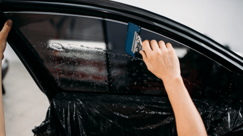 A man is applying car window tint on the inside.