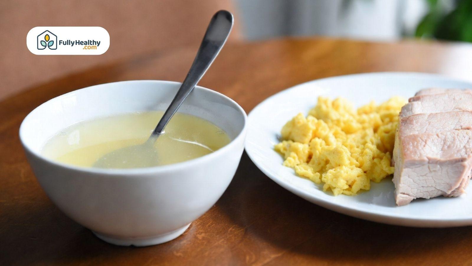 Light bone broth in a bowl served with scrambled eggs and sliced meat on a plate.