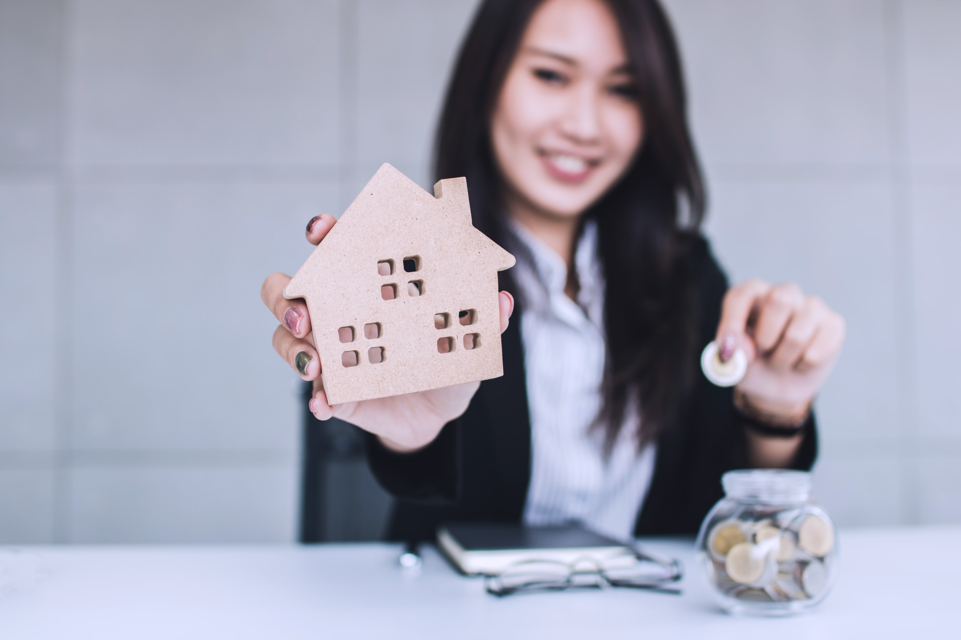 Save money for home concept, Business woman showing house wood model and put coins in jars, sunshine coast investment property investment