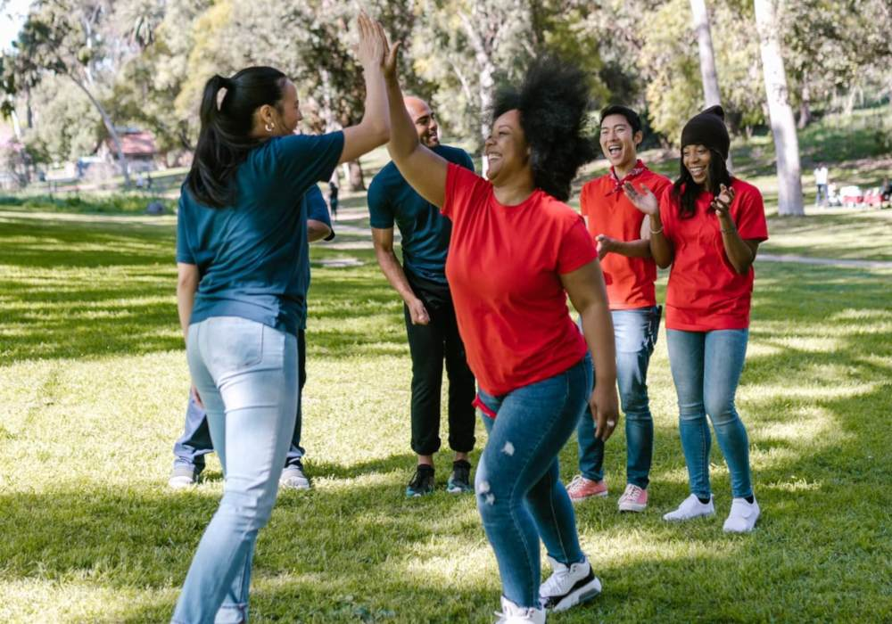 Two women high-five each other in a park surrounded by their team from a small business