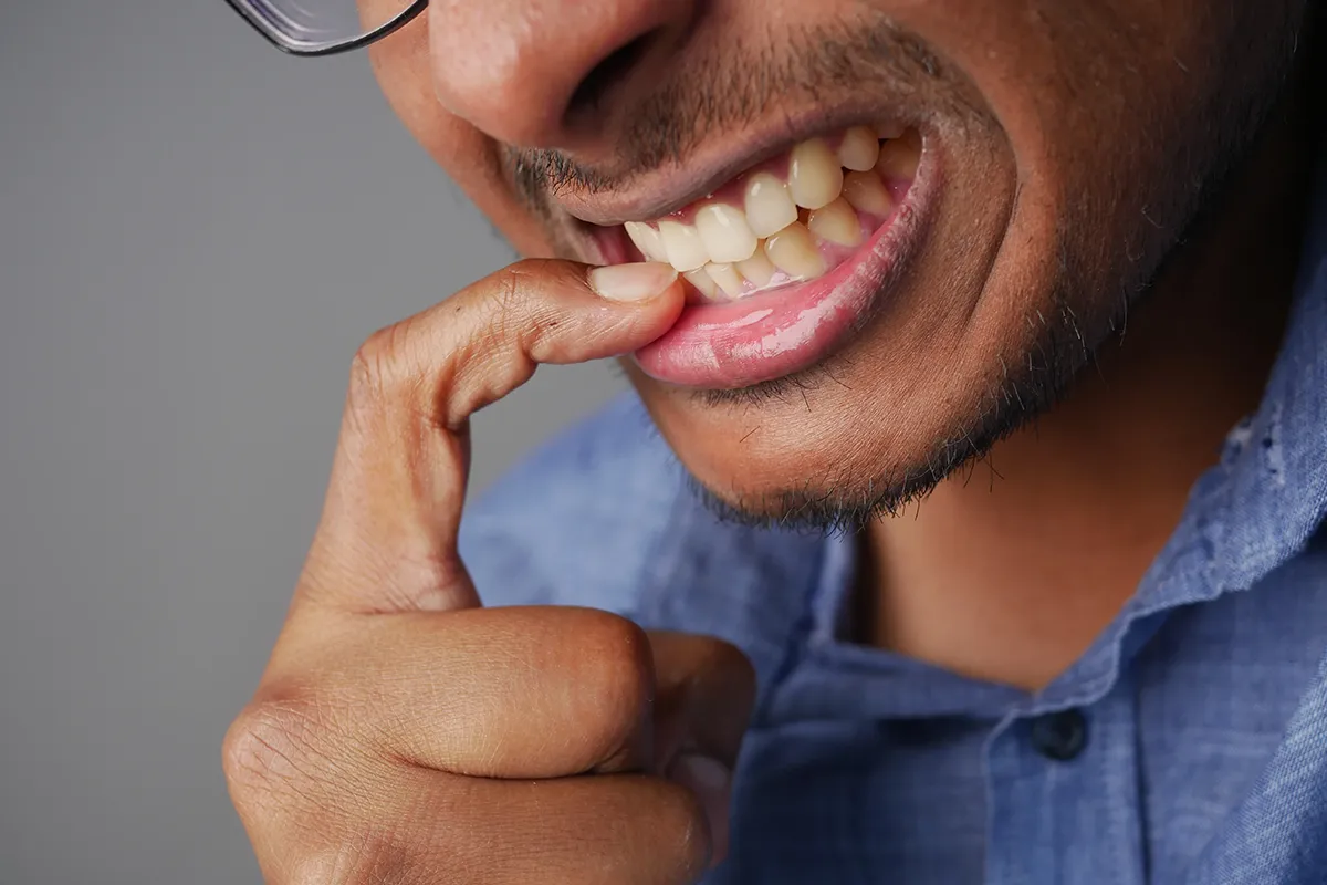 Close-up of person with glasses examining their teeth by pulling down lower lip with finger, showing healthy white teeth