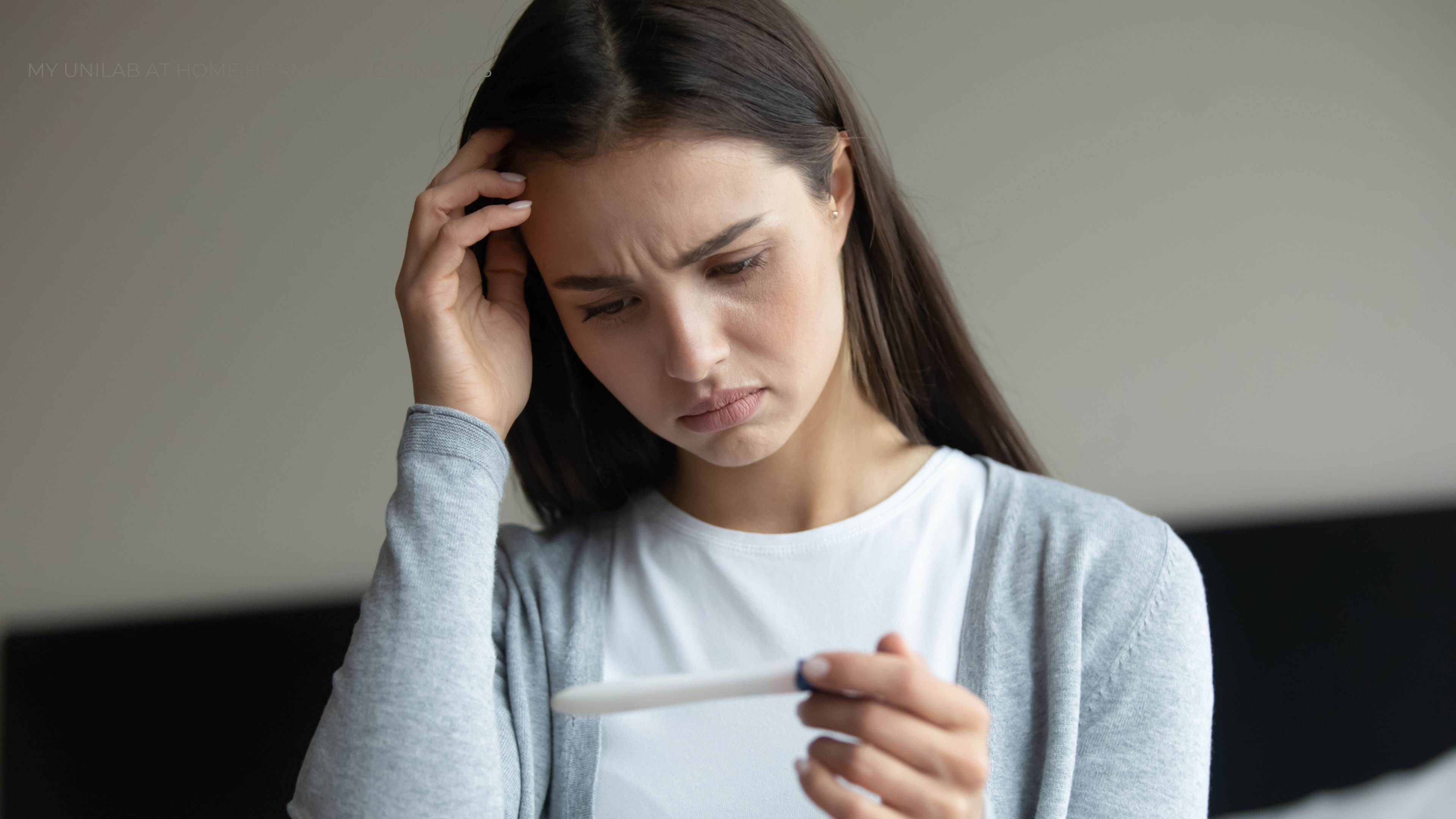Young female looking at a pregnancy test with a sad and confused look on her face.