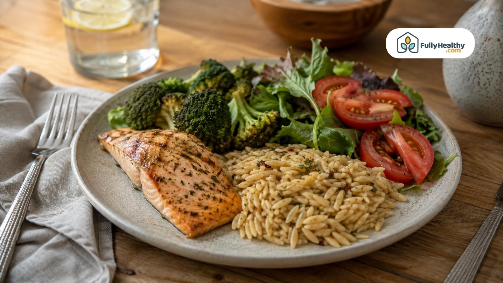 Grilled salmon served with orzo broccoli leafy greens and sliced tomatoes