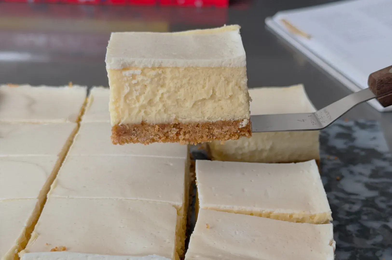 A slice of cheesecake being lifted from a tray, with several other slices in the background.