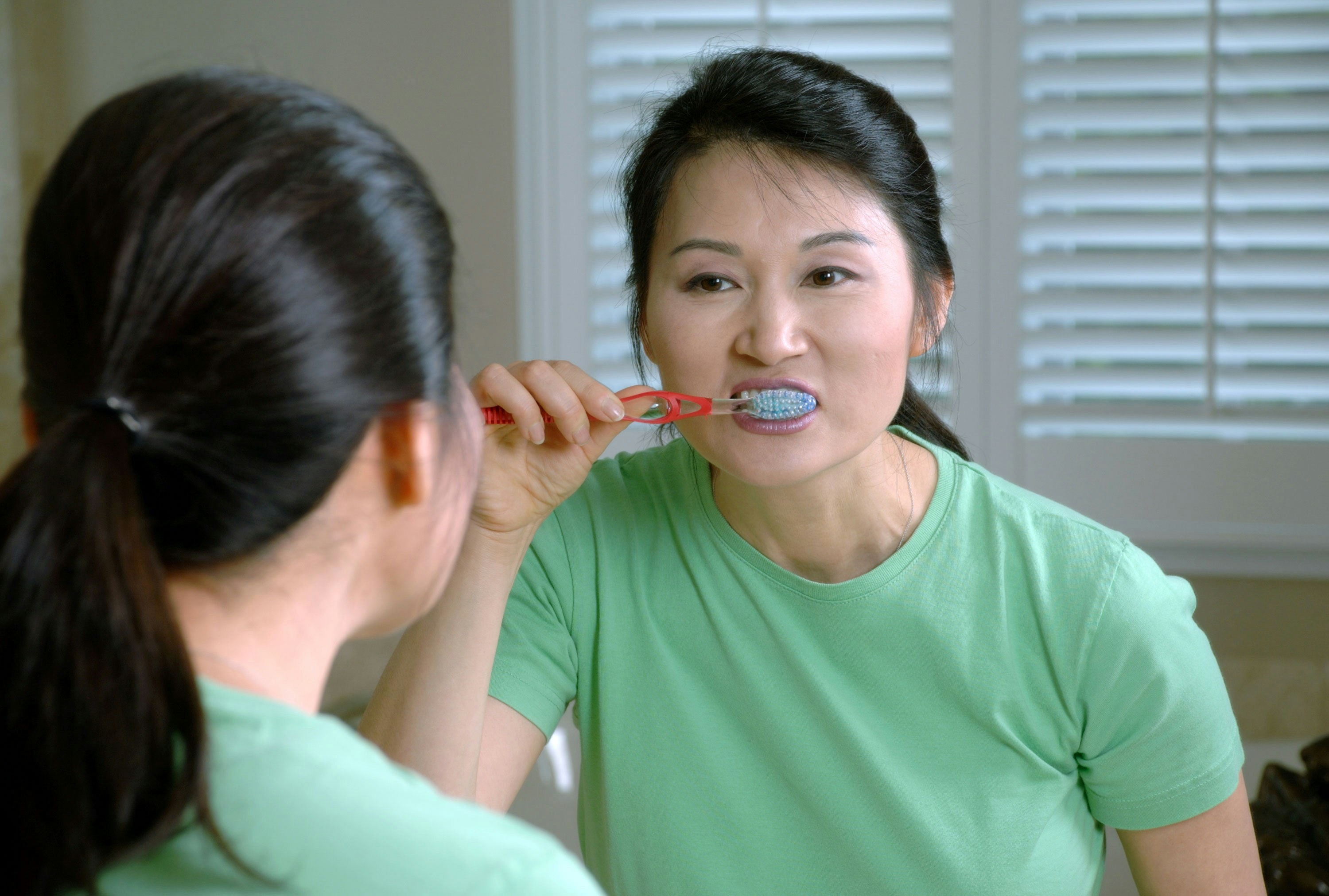 A person brushing their teeth at home, maintaining their new smile.
