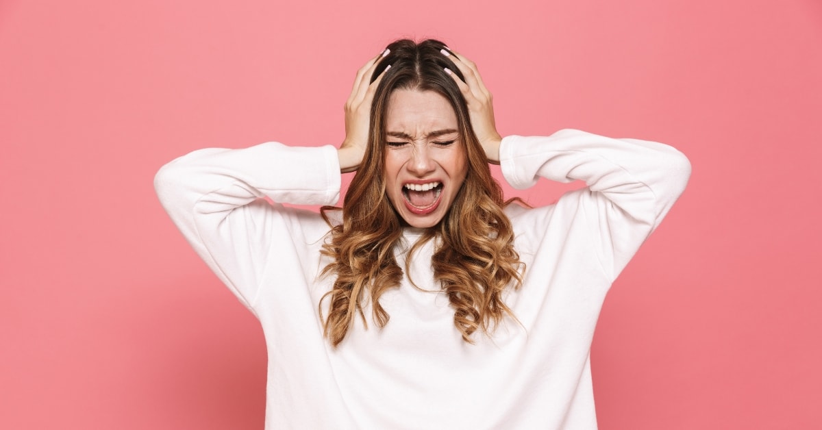 Frustrated woman in white sweater holding her head in stress, needs a tax fraud attorney for help.