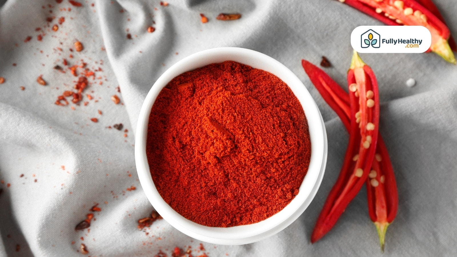 Ground chili powder in white bowl with sliced red chilies nearby