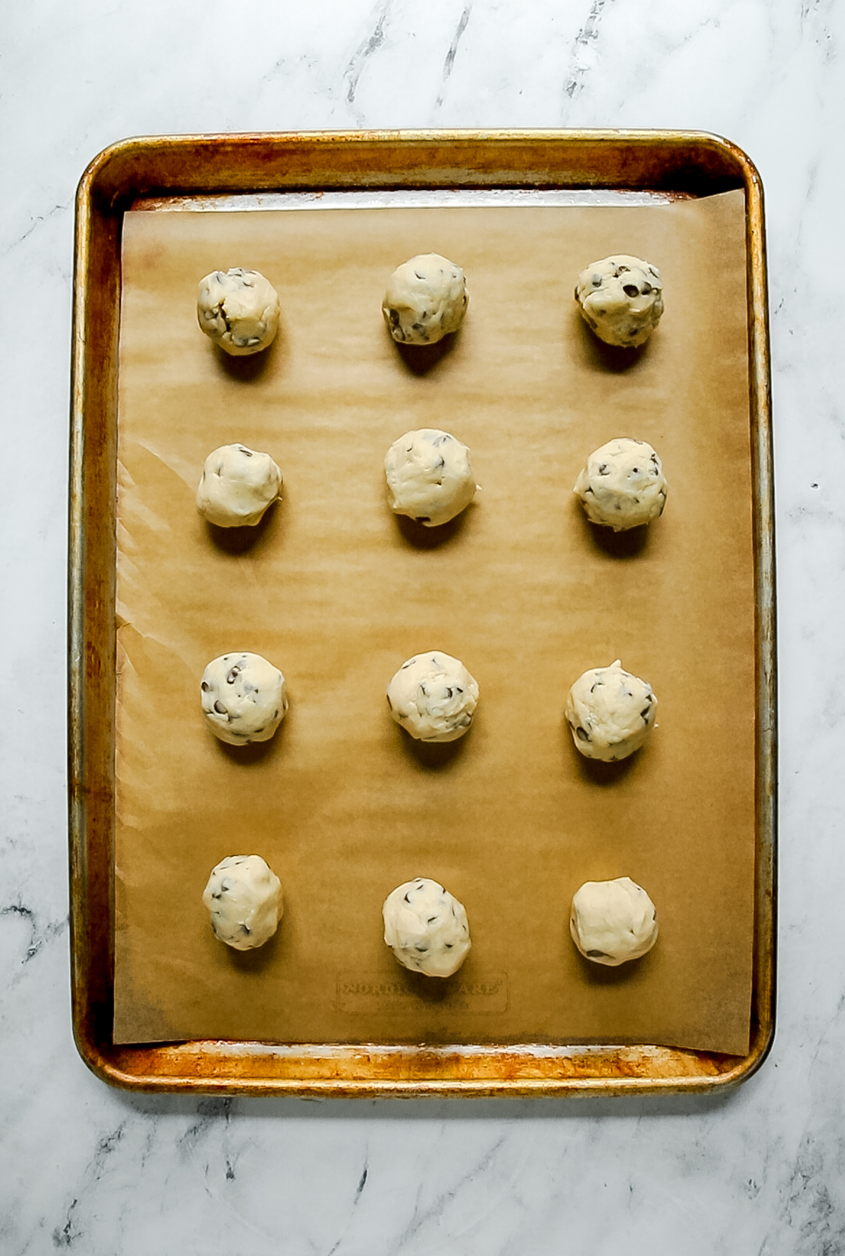 unbaked chocolate chip snowball cookie dough balls on baking sheet with parchment paper