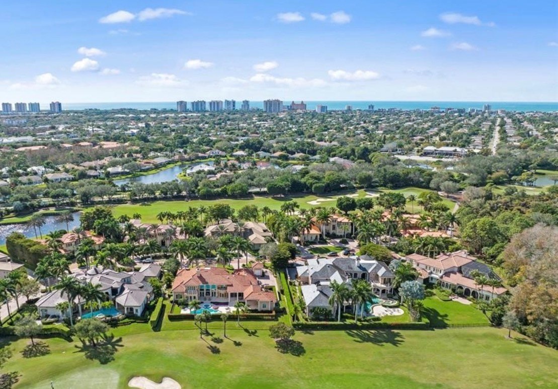 This image depicts a luxurious estate home situated in Pelican Marsh, Naples, with stunning golf course views and meticulously maintained landscaping. The property showcases high-end finishes and is surrounded by lush greenery, highlighting the serene lifestyle of this prestigious community.
