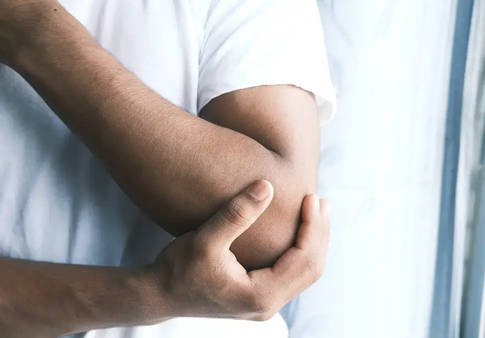 Person holding the inside of the elbow with visible discomfort near the forearm and elbow area.