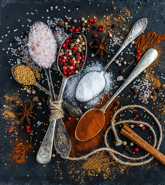 An image of several spoons, each filled with various spice and salts, such as table salt, Himalayan salt, and chili powder. 