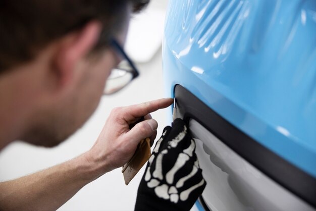 Close-up of a professional installer applying a blue car wrap around a vehicle’s edge using a precision tool, ensuring clean finish and fit.