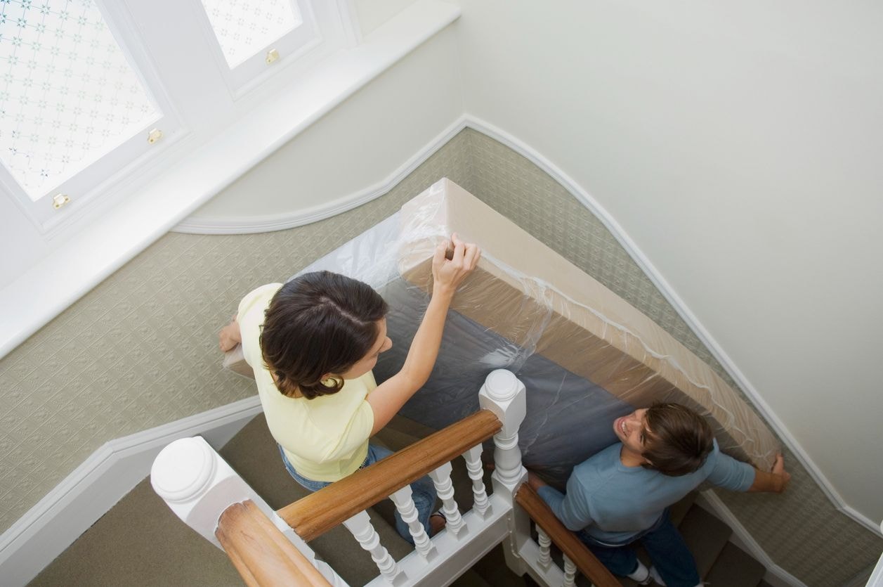 Man and woman lifting a foam mattress in a narrow space while carrying it upstairs during a move.