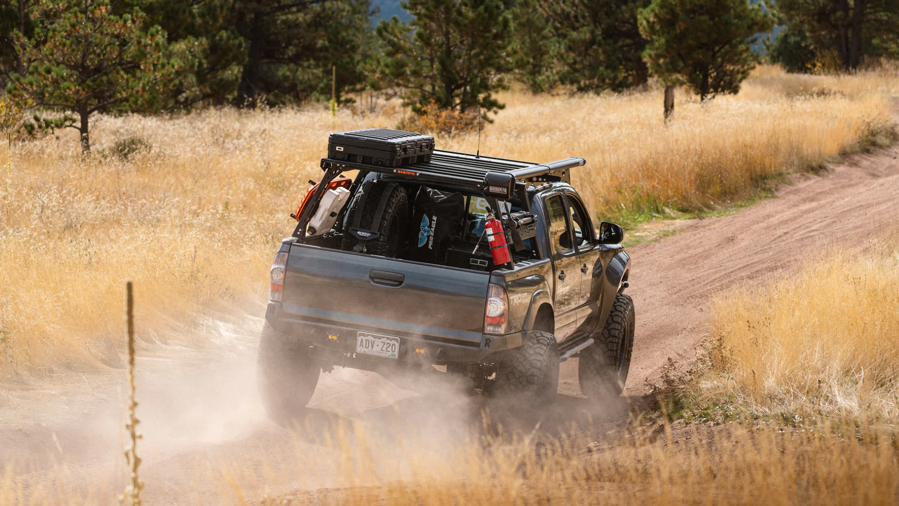 Sherpa Pak bed rack on grey Toyota Tacoma traveling away on a dirt road with gold grasses