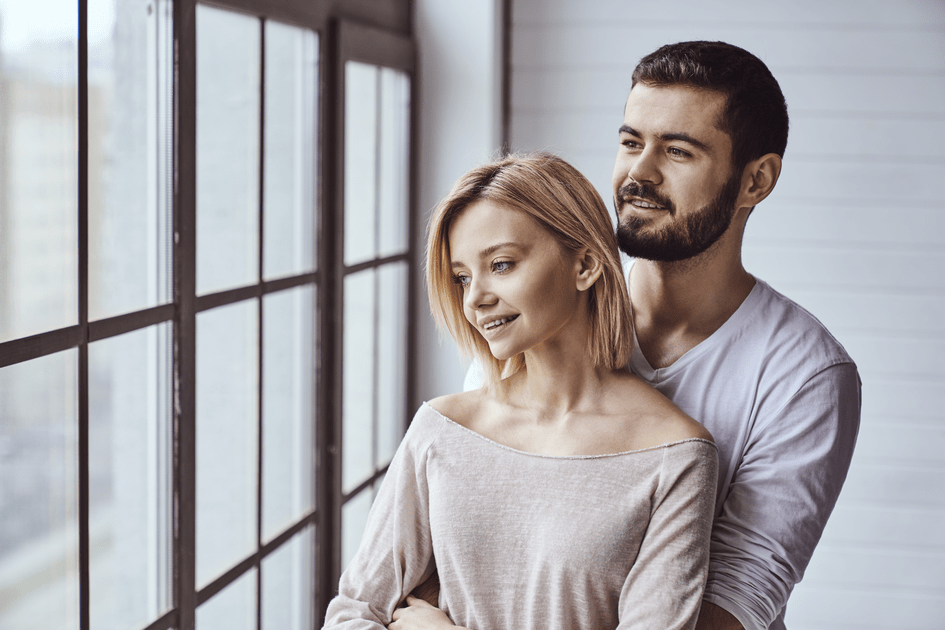 Couple embracing near window, feeling reassured after debunking common adult ADHD myths in marriage, fostering trust and open communication in their relationship.