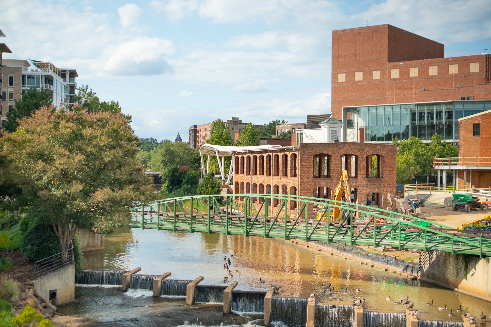 A scenic view of downtown Greenville, South Carolina, showcases the vibrant Falls Park and the iconic Liberty Bridge, surrounded by lush greenery and historic buildings, reflecting the area's charm and family-friendly atmosphere. This picturesque scene highlights the community's appeal for residents and visitors alike, making it one of the best places to live in Greenville County.