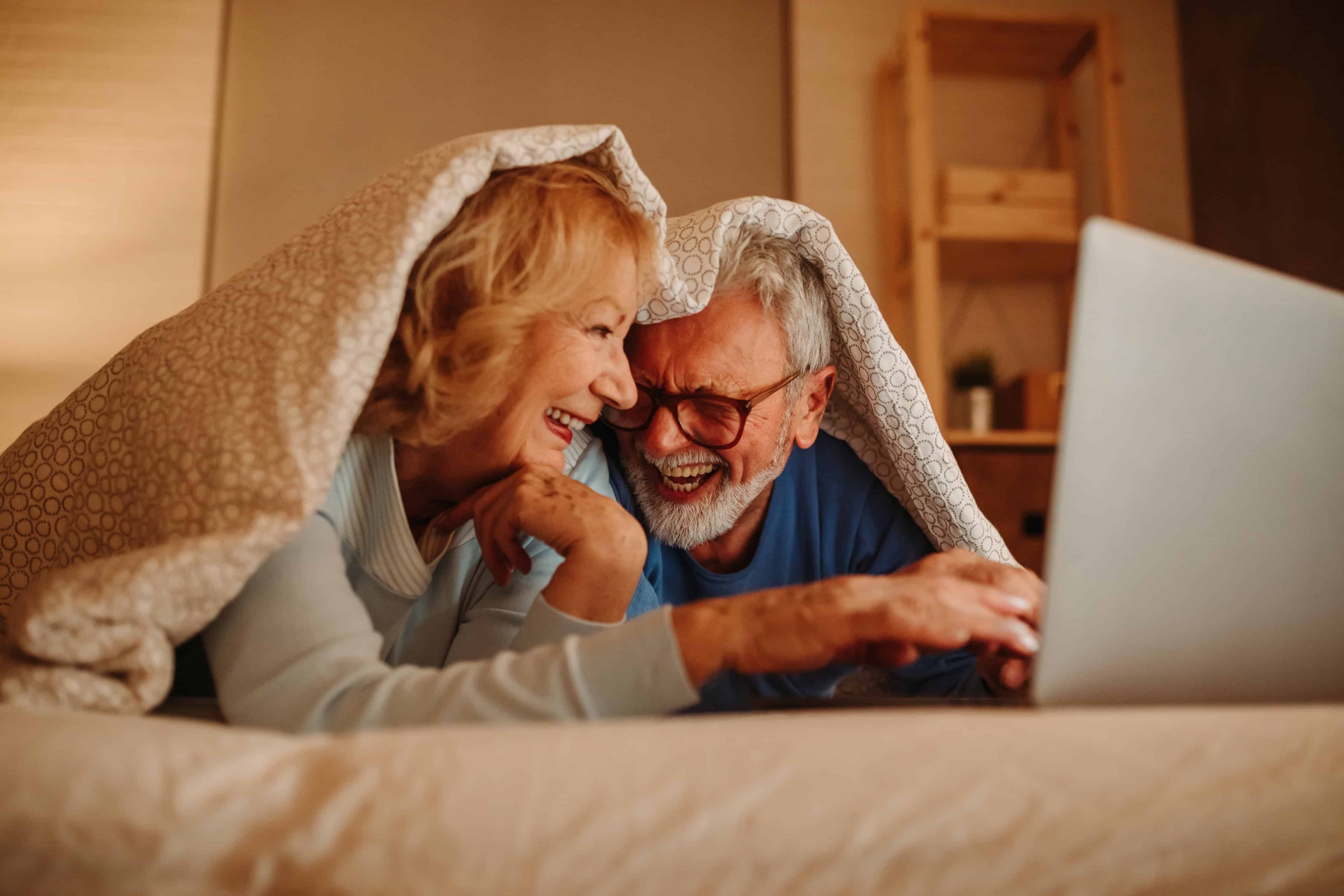 A couple in bed with a relaxing atmosphere, watching tv and laughing as they prepare to fall asleep.