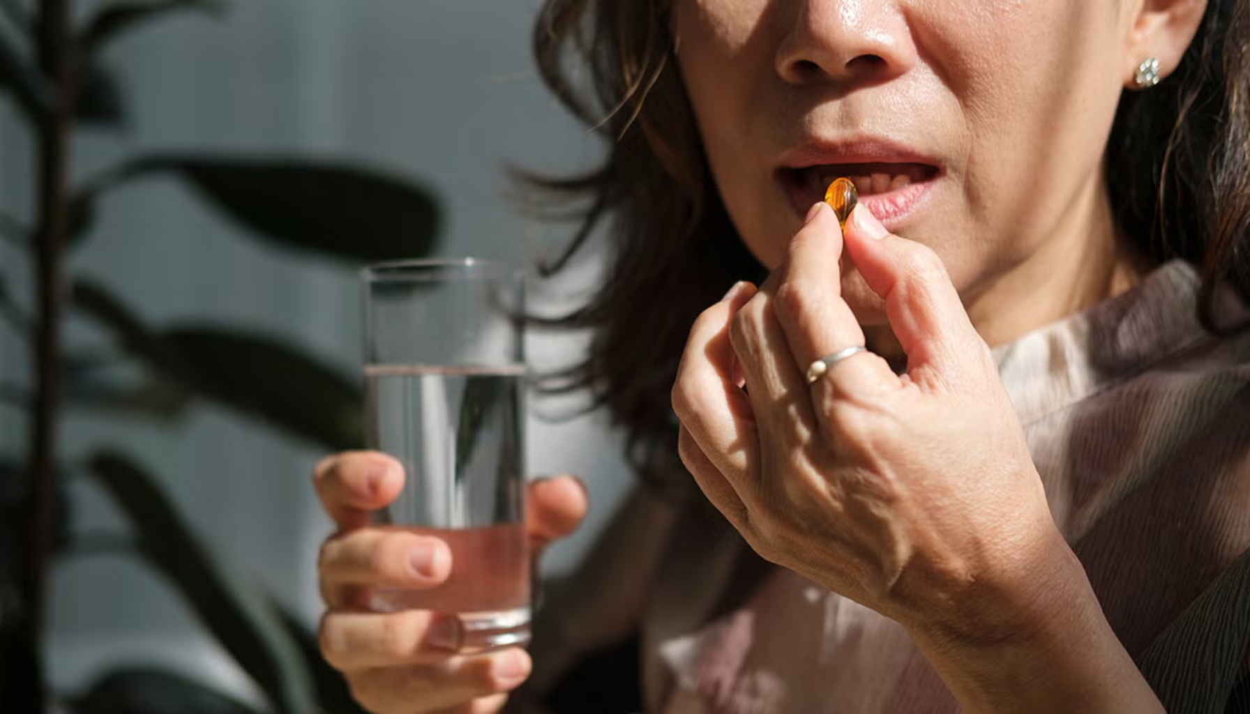 Vitamin D verdier – Hva er normalt og når bør du ta tilskudd? 13 Kvinne tar et kosttilskudd i form av en kapsel med et glass vann i hånden, i naturlig dagslys.