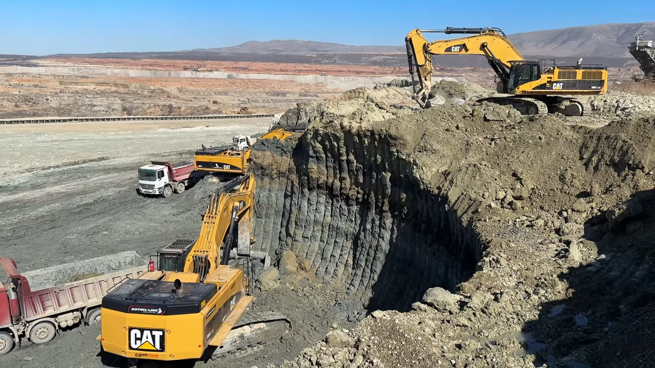 Several large yellow CAT excavators digging and moving dirt in a quarry with a red and white dump truck waiting to be loaded
