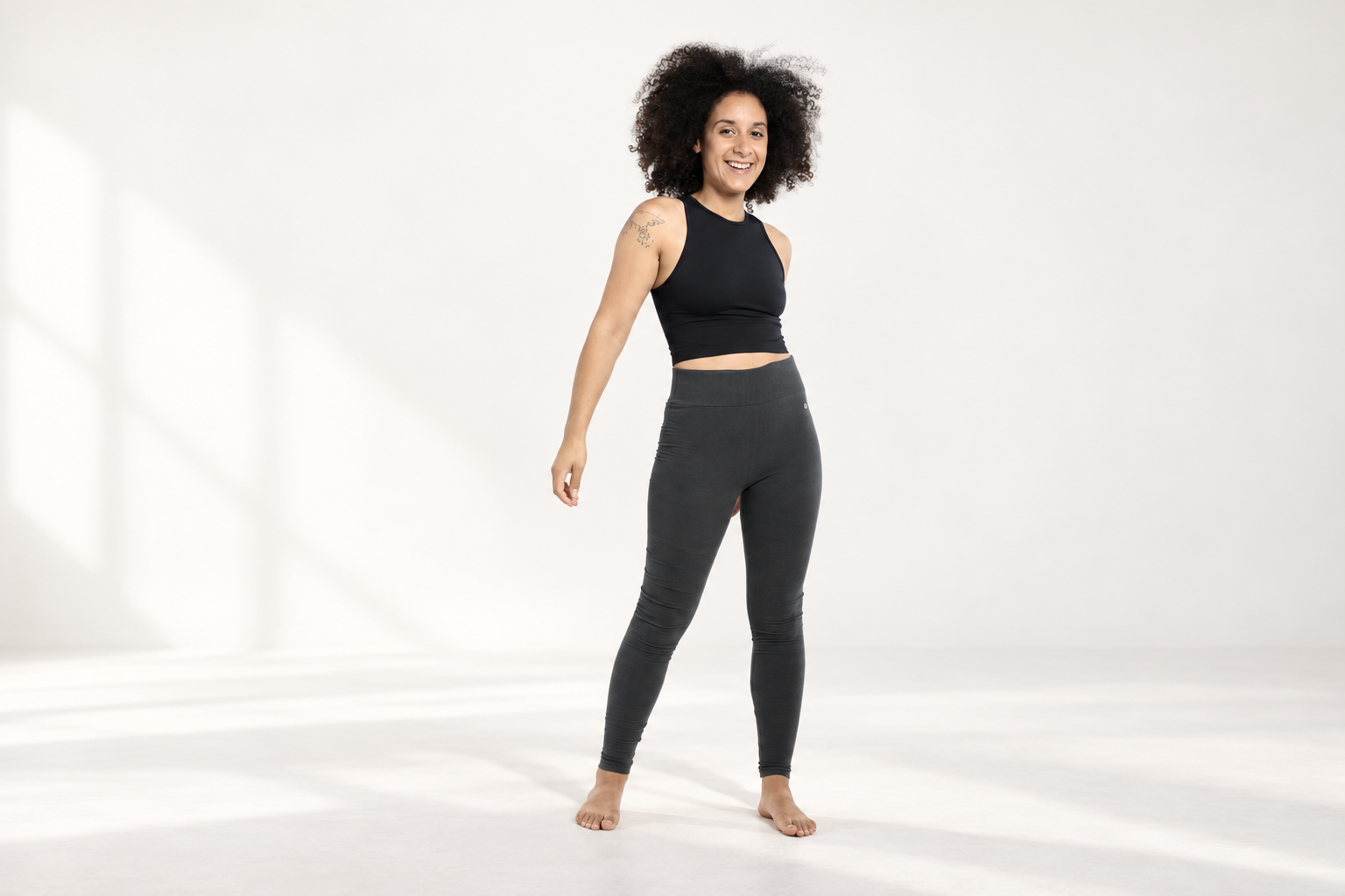 Woman wearing Orbasics dark grey leggings and a black top in a light studio.