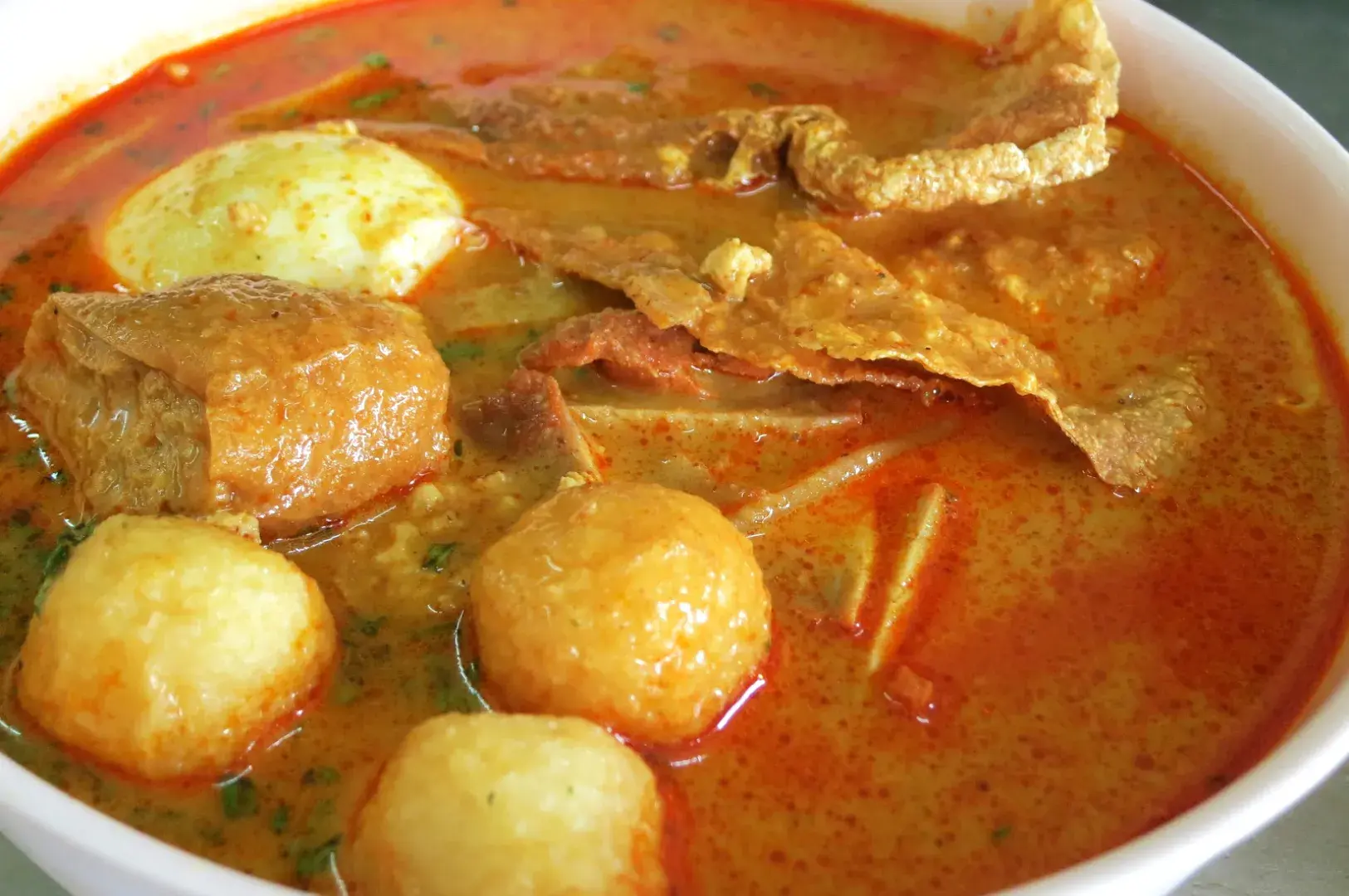 A bowl of spicy soup featuring meat pieces, a boiled egg, and round dumplings in a rich red broth.