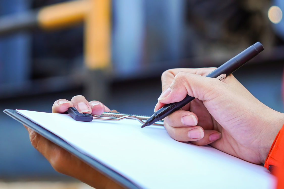 Close-up of a person writing on a clipboard during a supplement manufacturer prequalification review