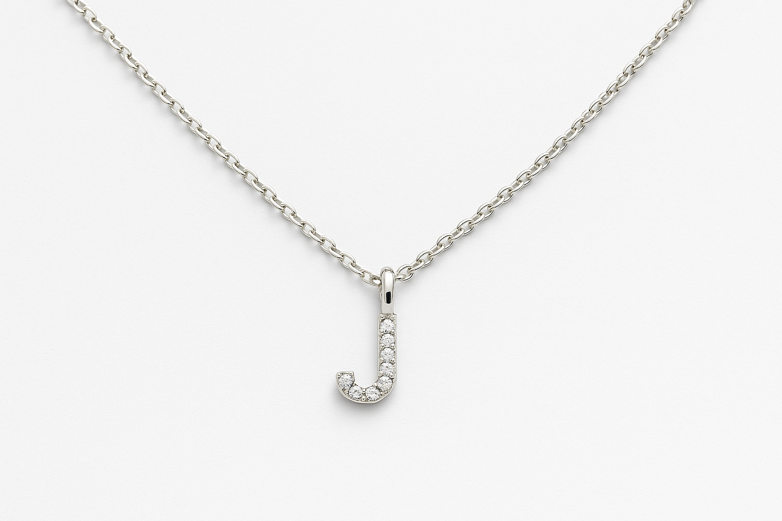 Balto aukso grandinėlė su blizgančiu raidelės pakabuku, papuoštu mažais deimantais, ant balto fono.