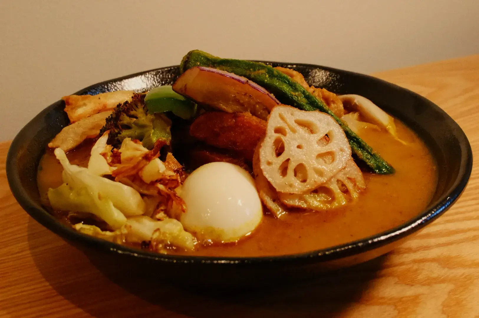 A bowl of curry with various vegetables, a sliced lotus root, and a soft-boiled egg.