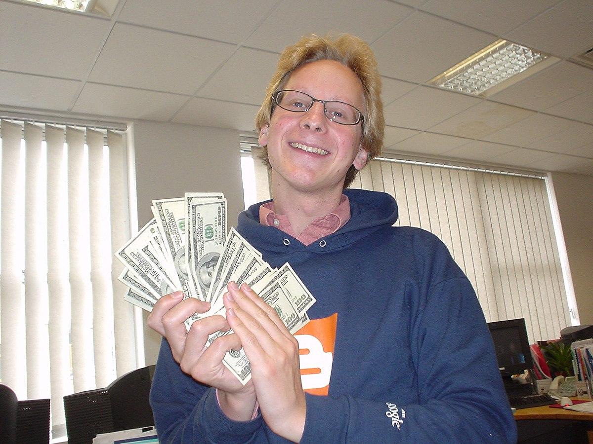 A man holding a stack of cash with a junk car in the background