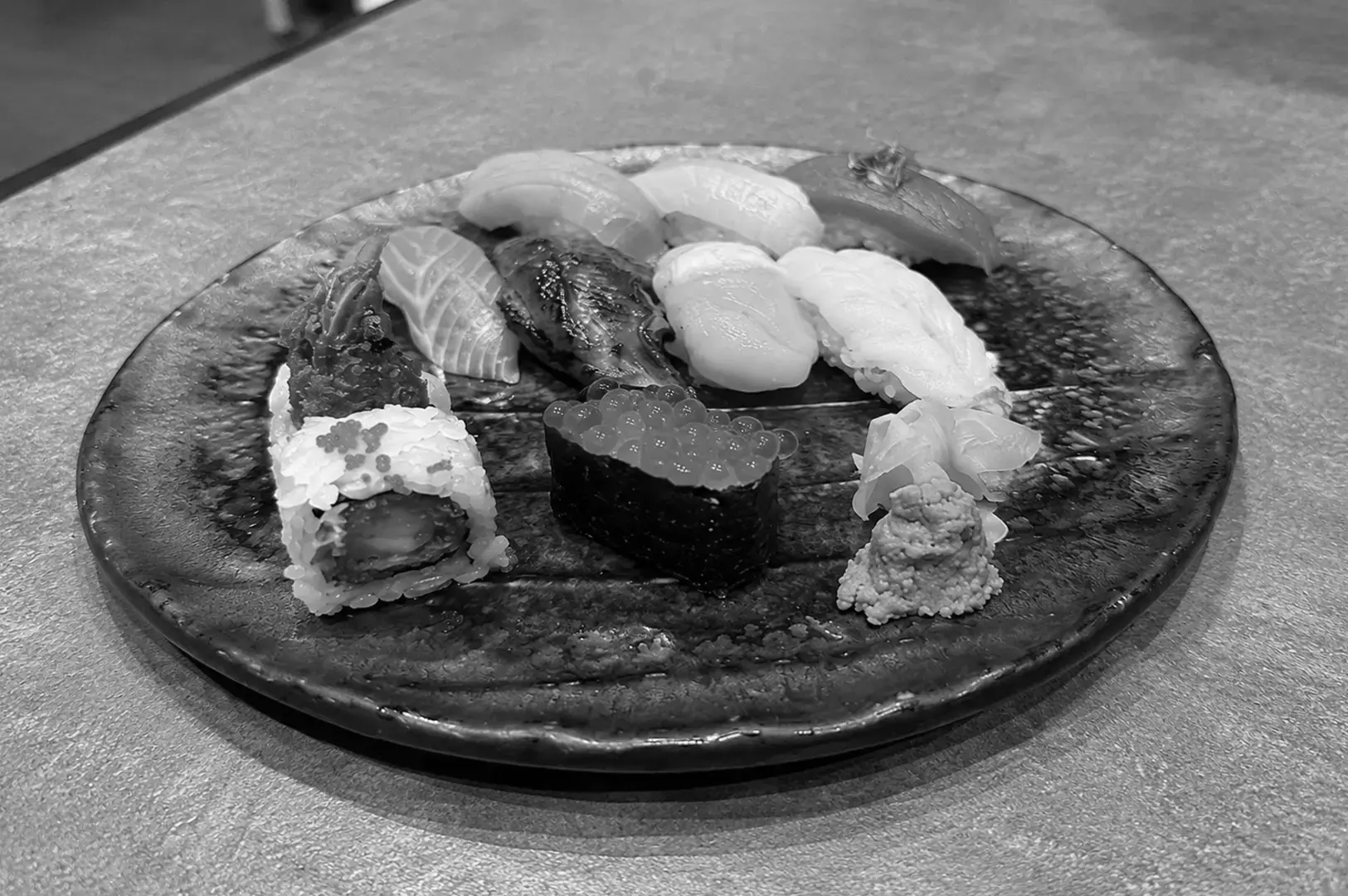 Assorted sushi platter with nigiri, sushi roll, salmon roe, and uni served on a ceramic plate.