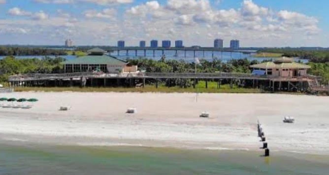 The image depicts a serene private beach park featuring soft white sand and crystal-clear blue water, perfect for relaxation and leisure. This exclusive coastal retreat is part of the Colony at Pelican Landing, offering residents world-class amenities and a luxurious lifestyle in Bonita Springs, FL.