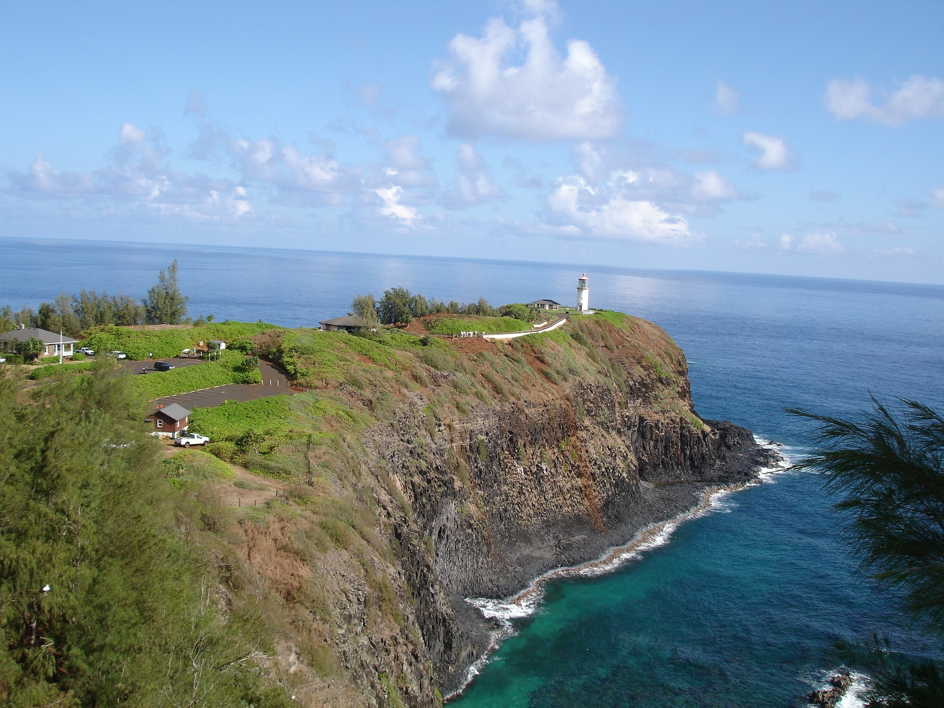An aerial view of Kilauea Lighthouse in Kauai. A lighthouse is visible on land by the sea with green plants.