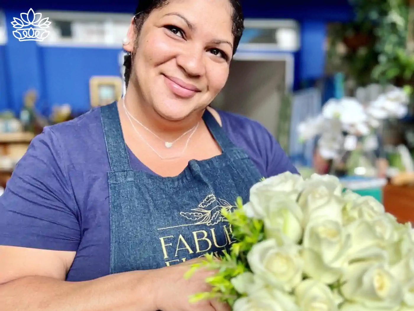 A cheerful florist in a blue apron proudly presenting a bouquet of white roses, embodying expert craftsmanship in floral design. Fabulous Flowers and Gifts: Flower Arrangements Under R500, Delivered with Heart.